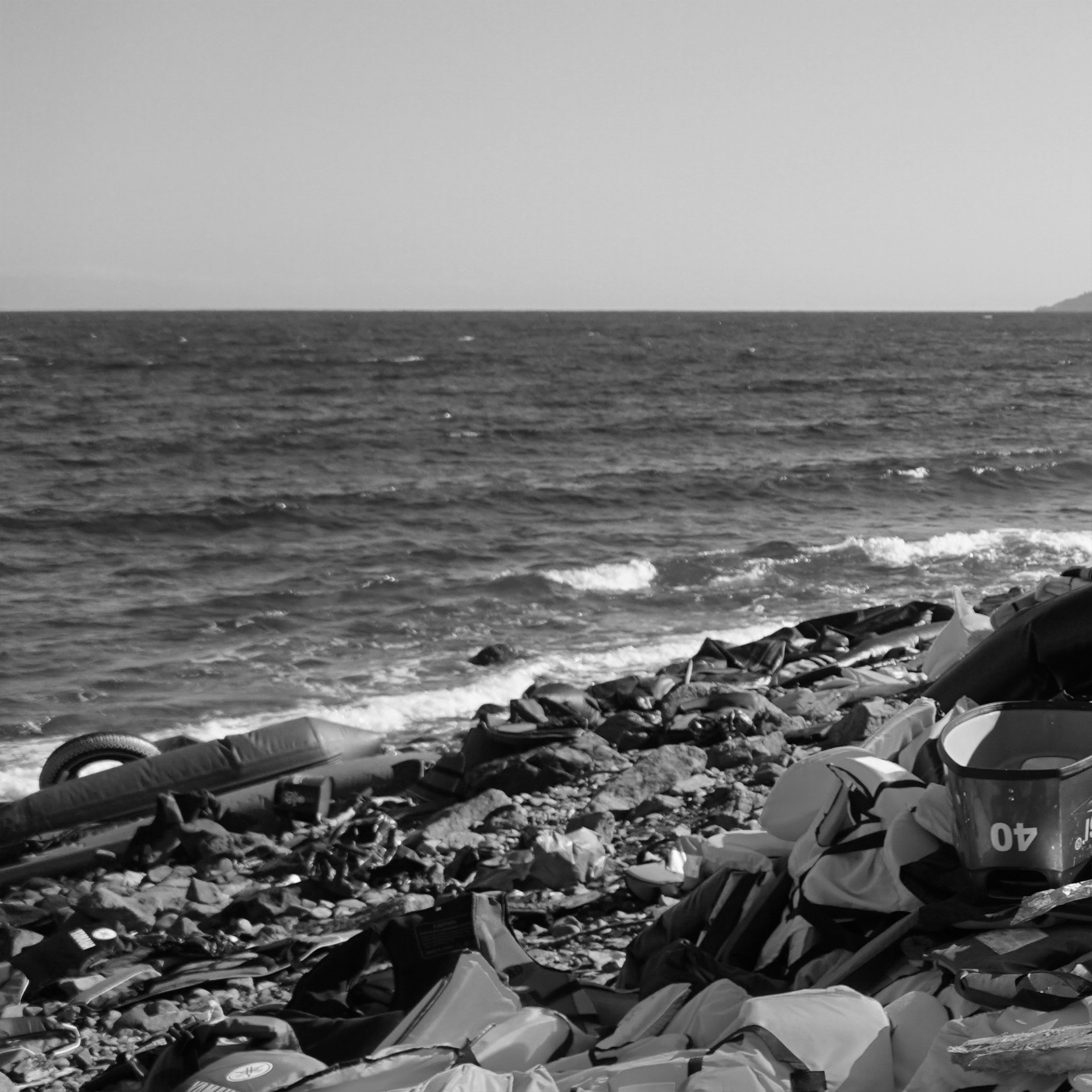 Schwarz-Weiß-Fotografie eines Strandes mit zahlreichen Rettungswesten und -reifen